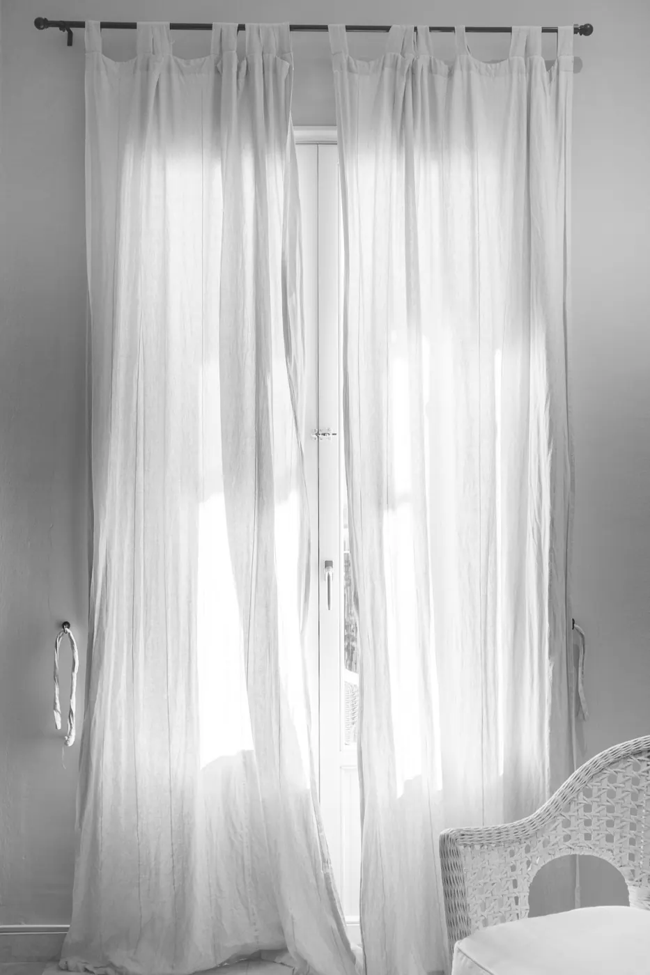 White sheer curtains hanging from a black curtain rod beside a window