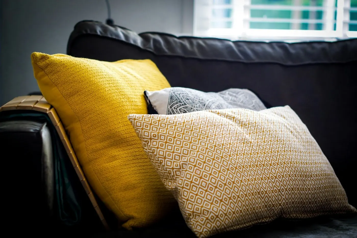 Yellow, grey and textured cream cushions on a dark sofa