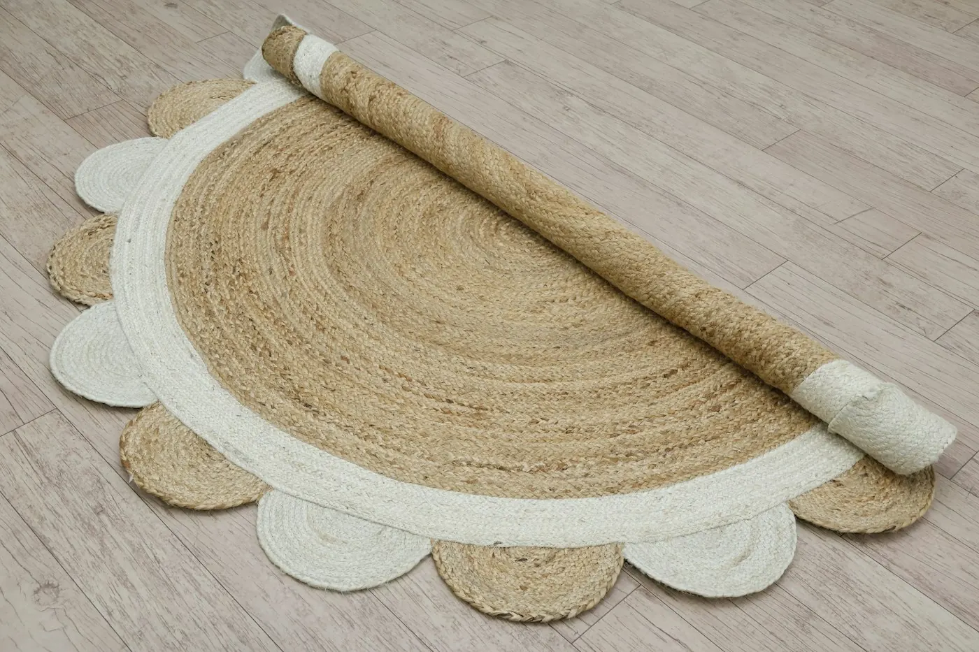 Half-rolled round jute rug with a scalloped white border on a wooden floor