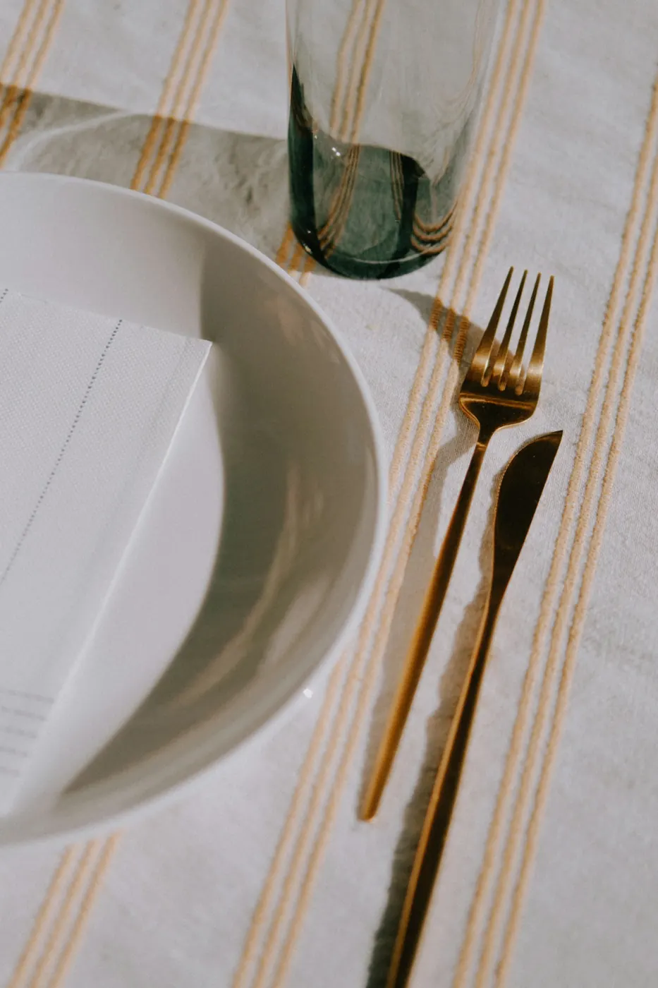 Striped table linen with a white plate and gold cutlery